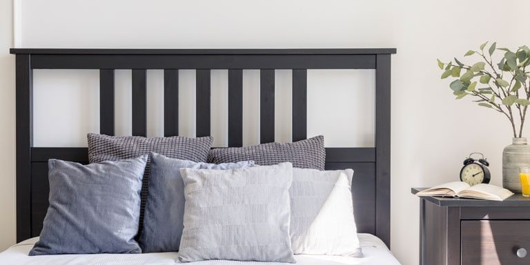 Grey and white pillows on bed with black headboard in simple bedroom interior. Real photo